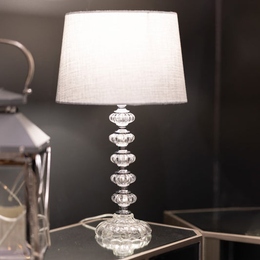 Decorative table lamp with a glass base and grey shade on a dark surface.