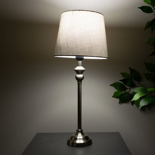 Table lamp with a grey shade on a dark surface against a neutral background
