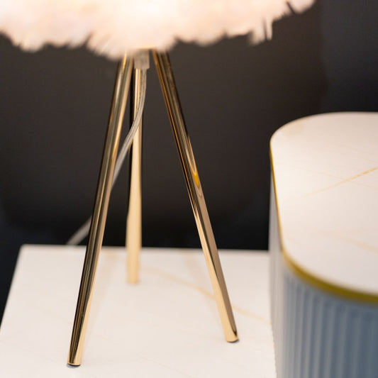 Close-up of a gold tripod lamp with a soft white shade on a dark background