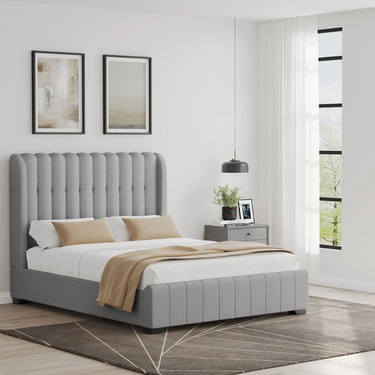 Grey upholstered bed in a modern bedroom with white walls and large windows.