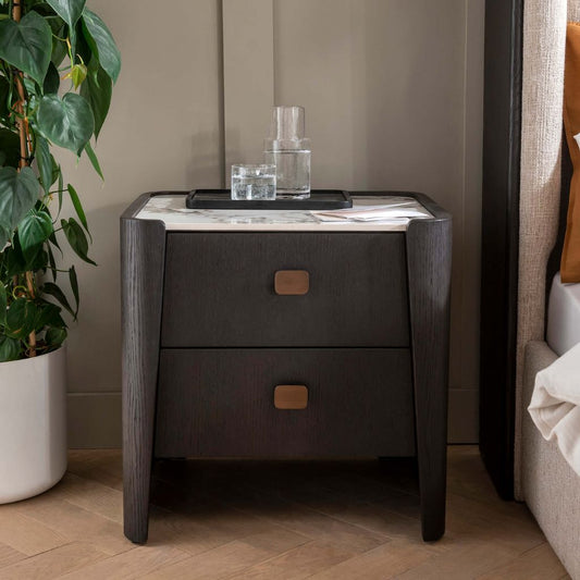 Dark wooden nightstand with marble top next to a plant and bed.