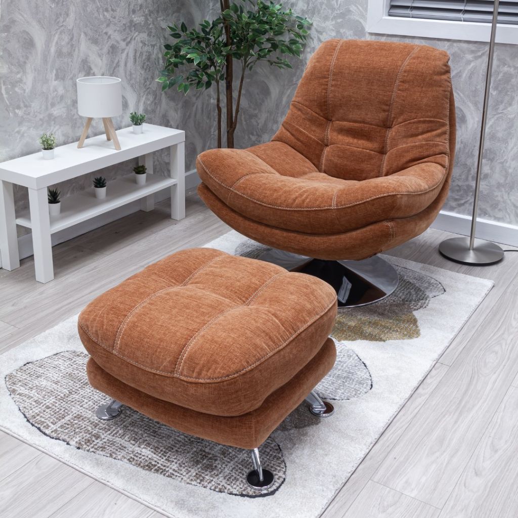 Brown lounge chair and ottoman on a rug with a white table and plants in the background.