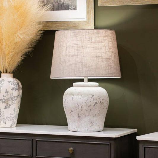 Table lamp with textured shade on a wooden surface against a green wall.