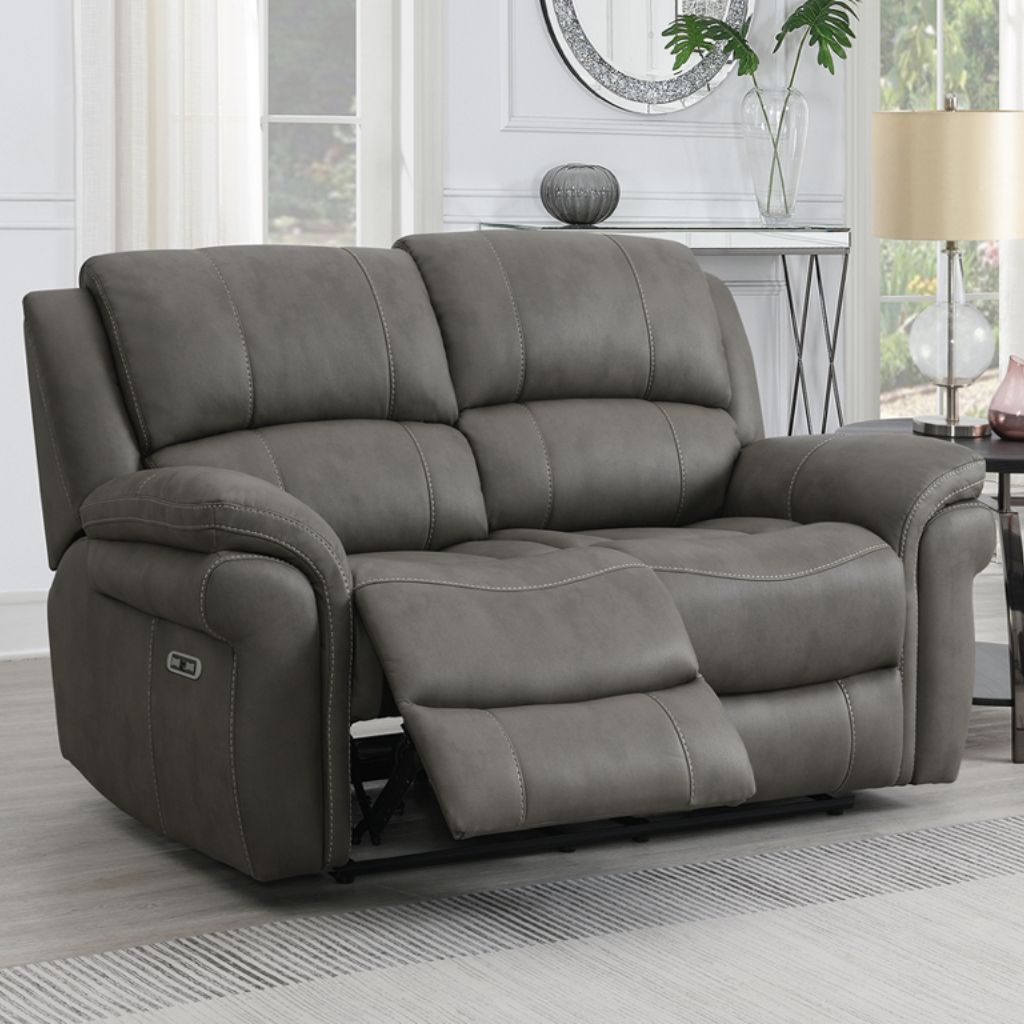 Gray reclining sofa in a living room setting with a lamp and window in the background.