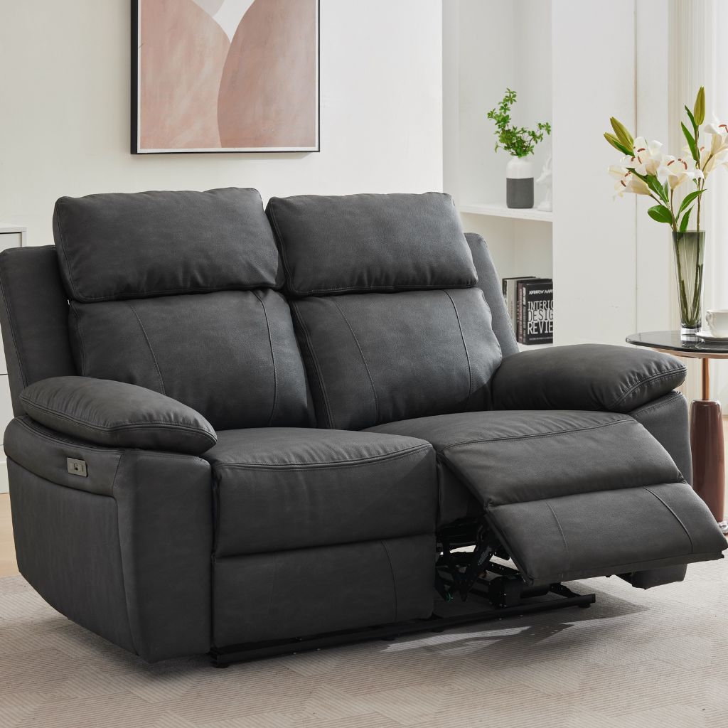 A dark grey two-seater reclining sofa shown in a living room setting with one seat cushion extended.