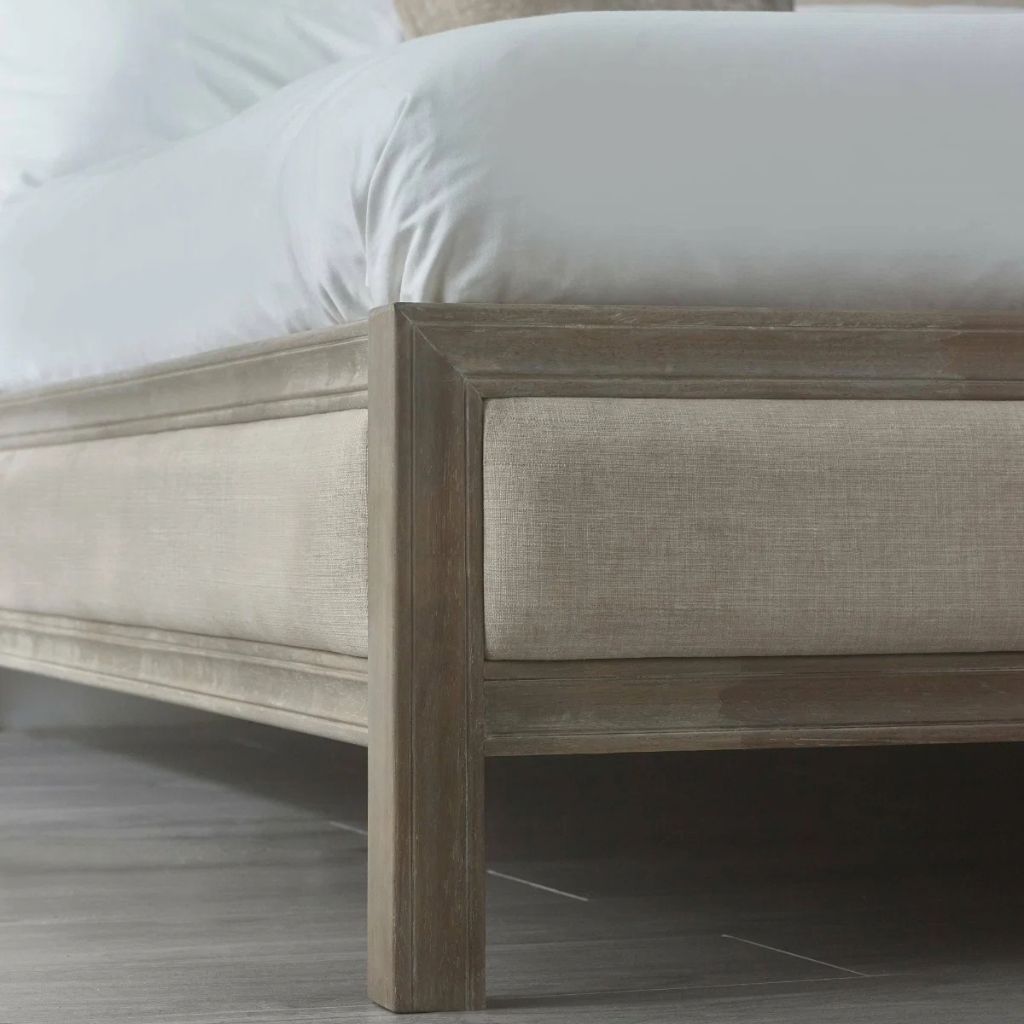 Close-up of a bed frame corner with a ivory upholstered side rail and a limed oak wooden frame.