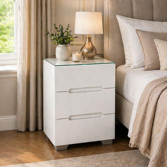 White nightstand with glass top next to a bed in a bedroom setting