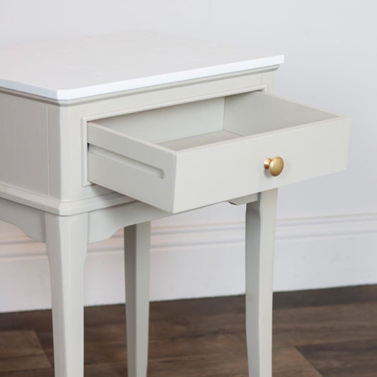 Stone side table with a drawer and gold handle on a wooden floor.