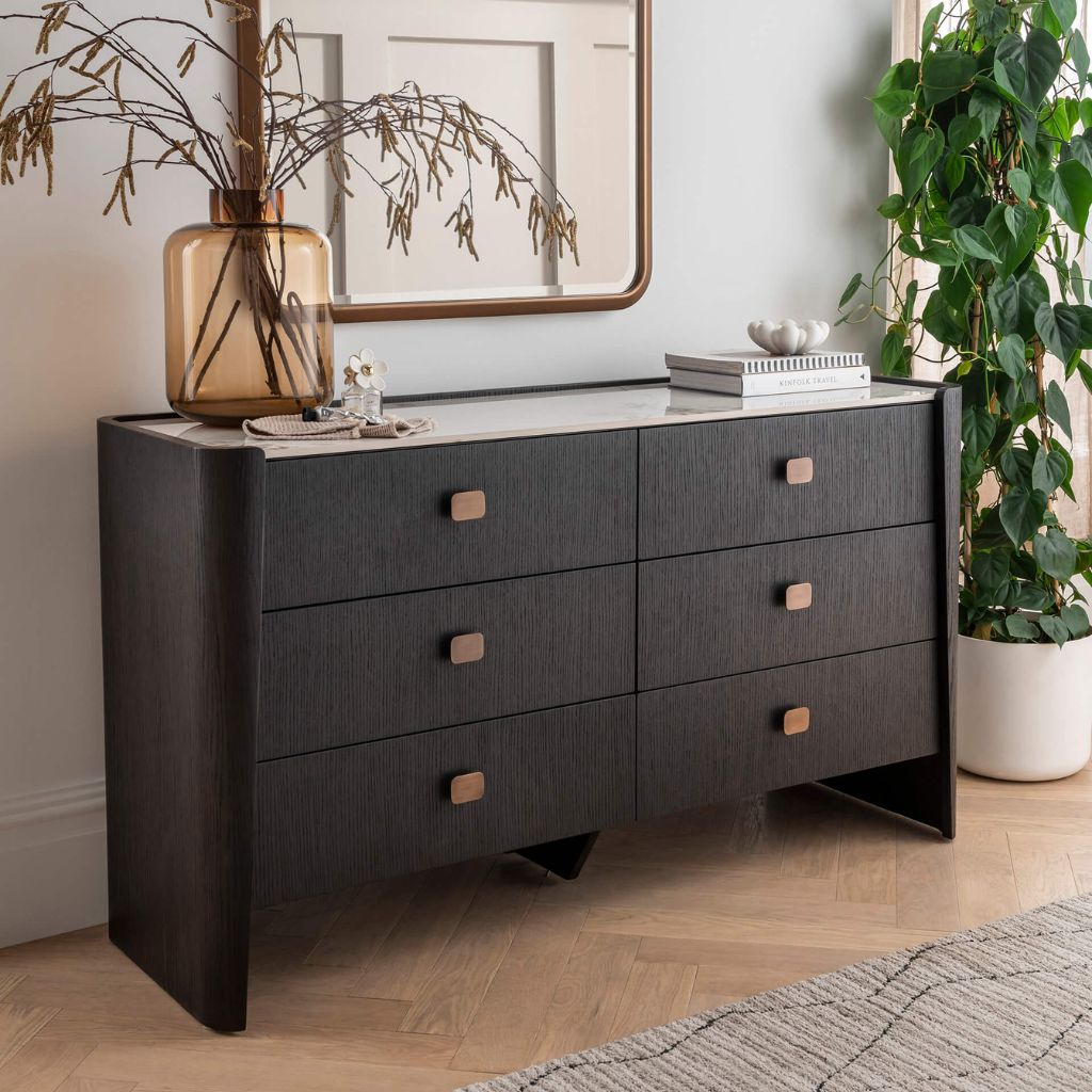 Dark wood dresser with six drawers in a room with a plant and mirror.